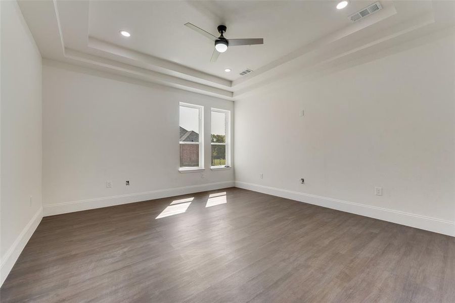 Spacious room featuring a tiered tray ceiling with recessed lighting and a ceiling fan Spacious room featuring a tiered tray ceiling with recessed lighting and a ceiling fan