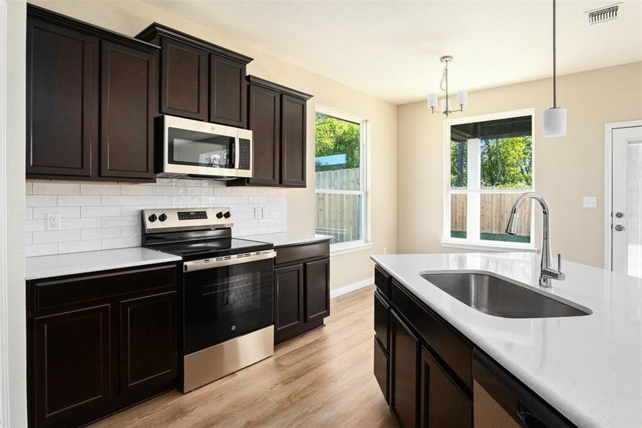 Kitchen with appliances with stainless steel finishes, light quartz countertops, and light wood-style flooring