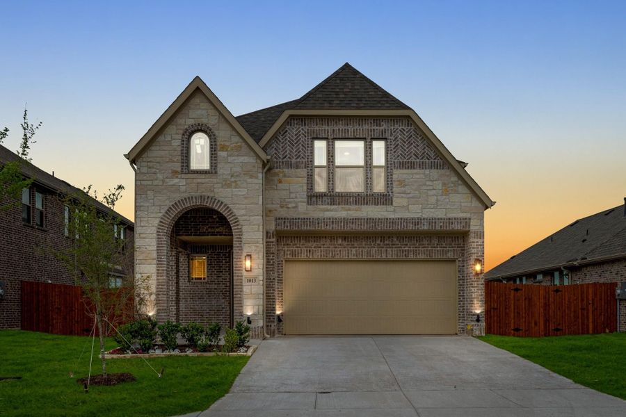 Two-story brick and stone home with arched entry, two-car garage, and concrete driveway at dusk