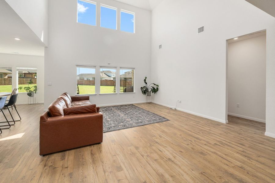 Bright living space featuring vaulted ceilings, wood-finish flooring, and multiple windows providing natural illumination Bright living space featuring vaulted ceilings, wood-finish flooring, and multiple windows providing natural illumination