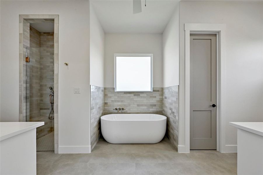 Extensive custom tile work around the free standing soaking tub and private shower behind frameless glass.
