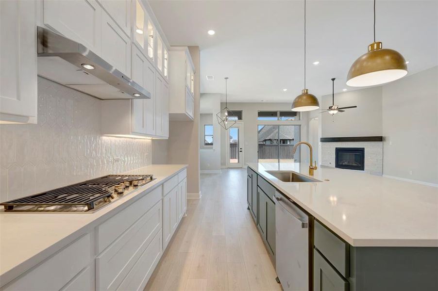Kitchen featuring a glass covered fireplace, dual tone cabinetry, light wood finished floors, open floor plan, and stainless steel appliances Kitchen featuring a glass covered fireplace, dual tone cabinetry, light wood finished floors, open floor plan, and stainless steel appliances