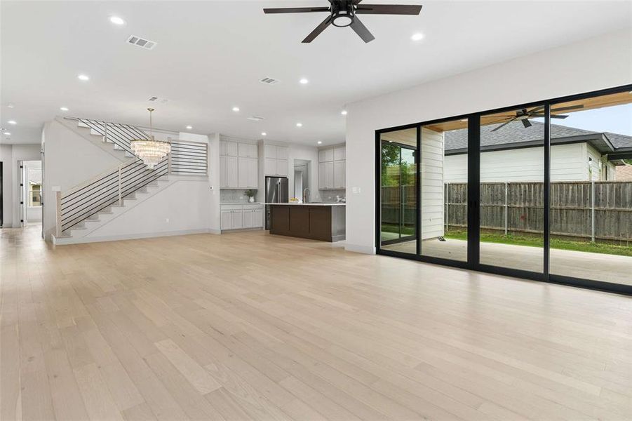 Spacious open-concept living area featuring light wood-finish flooring, a contemporary chandelier over the staircase, and a modern kitchen with a large island. Nine foot sliders lead to the private covered patio. Spacious open-concept living area featuring light wood-finish flooring, a contemporary chandelier over the staircase, and a modern kitchen with a large island. Nine foot sliders lead to the private covered patio.