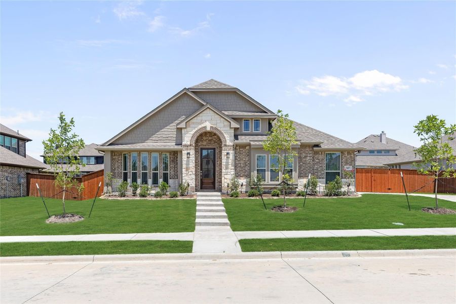 Single-story brick and stone home with arched entry, large front lawn, and young trees lining the walkway.
