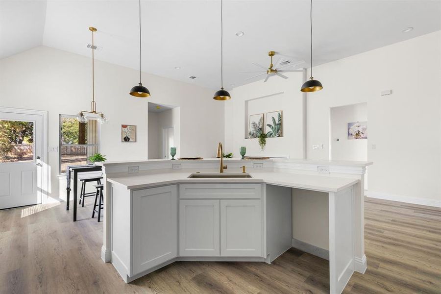 Kitchen with light hardwood / wood-style flooring, hanging light fixtures, sink, and a kitchen island with sink