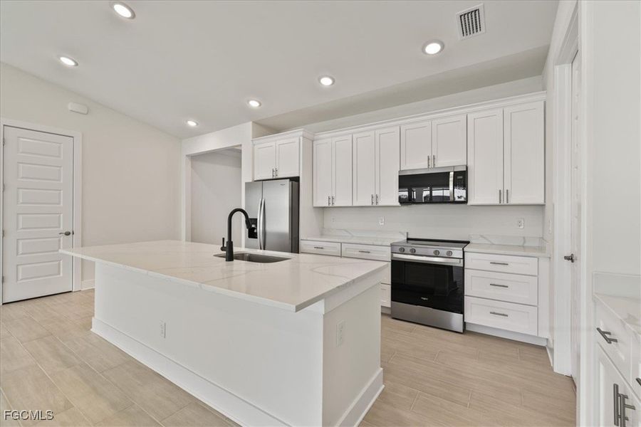 Kitchen featuring stainless steel appliances, a kitchen island with sink, white cabinets, wood tiled floors, and light stone countertops Kitchen featuring stainless steel appliances, a kitchen island with sink, white cabinets, wood tiled floors, and light stone countertops