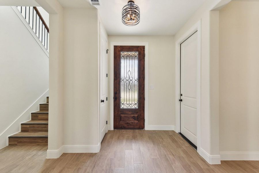 Foyer with stairway, light wood-style flooring, visible vents, and baseboards