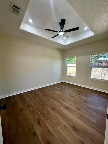 Recessed tray ceiling with a black ceiling fan and integrated lighting, wood-finish flooring, and two windows