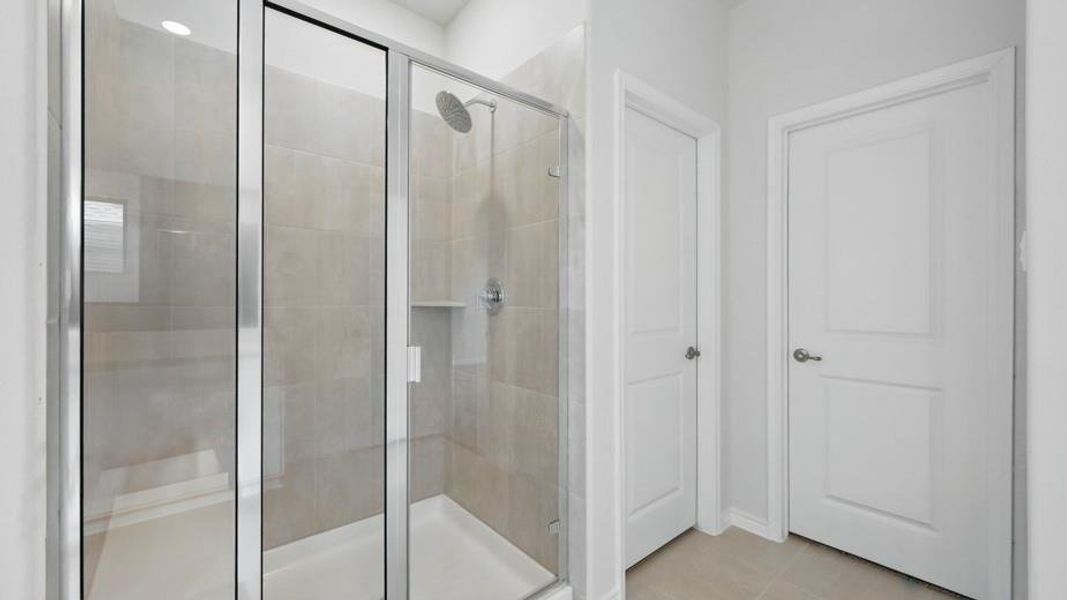Walk-in shower featuring a rain showerhead, built-in shelving, and light-toned tile surround