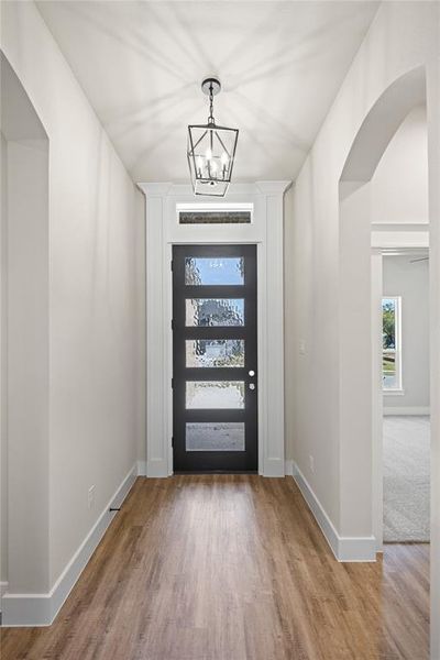 Foyer entrance with arched walkways, light wood-type flooring, and a chandelier