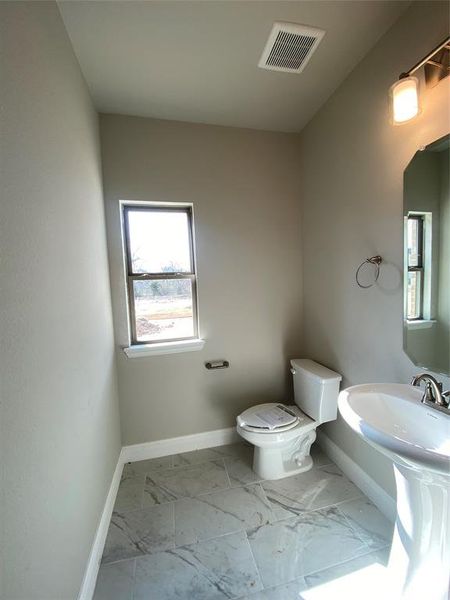 Powder bath with pedestal sink, window, and oversized 12x24 marble-style tile floors.