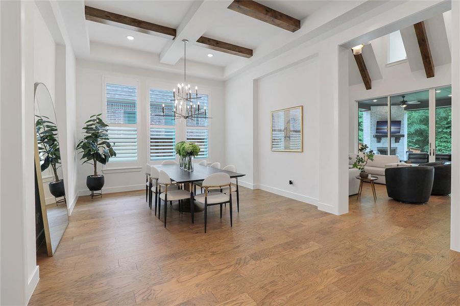 Spacious dining area featuring wood-finish flooring, a coffered ceiling with exposed wood beams, and a contemporary chandelier