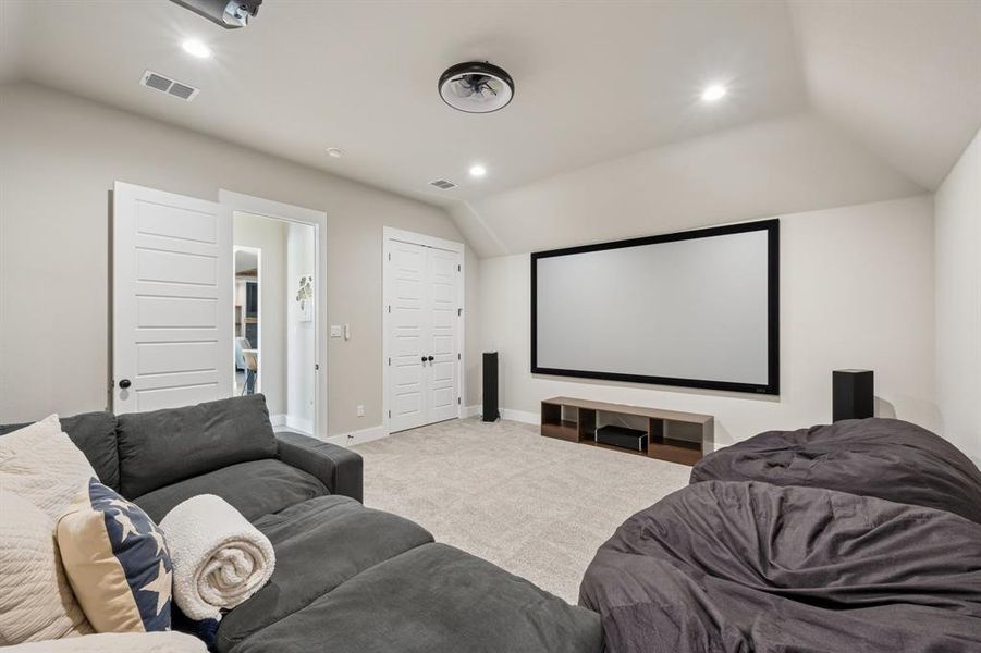 Carpeted home theater room with vaulted ceiling and recessed lighting