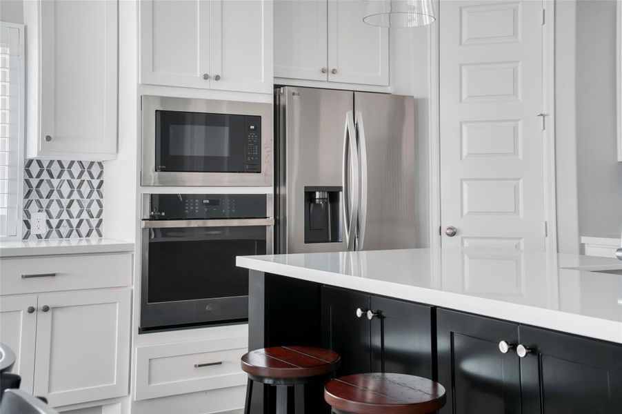 This modern kitchen features sleek white cabinetry, stainless steel appliances including a double oven and fridge, a stylish geometric backsplash, and a spacious island with seating, perfect for entertaining. This modern kitchen features sleek white cabinetry, stainless steel appliances including a double oven and fridge, a stylish geometric backsplash, and a spacious island with seating, perfect for entertaining.