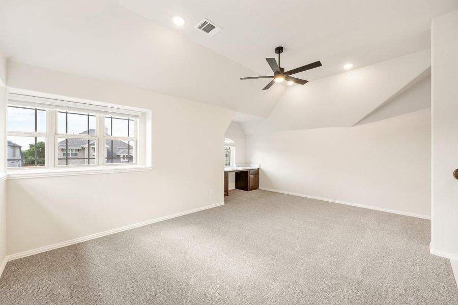 Spacious empty room with vaulted ceiling, ceiling fan, carpet flooring, and built-in desk area