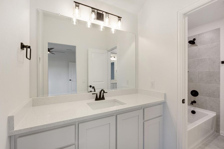 Bathroom with white quartz vanity, large mirror, and tiled tub-shower combo with dark fixtures