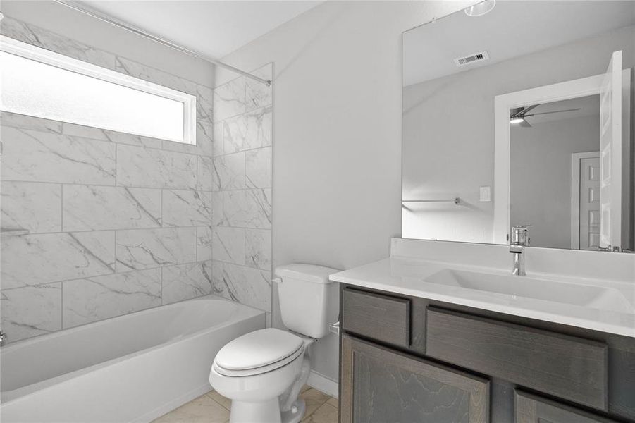 Secondary bath features tile flooring, bath/shower combo with tile surround, wood stained cabinets, beautiful light countertops, mirror, dark, sleek fixtures and modern finishes!