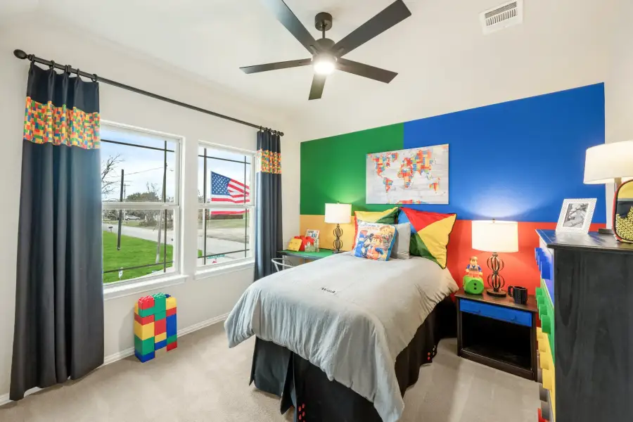 Children's bedroom with colorful Lego-themed accent wall, ceiling fan, and large windows with navy curtains