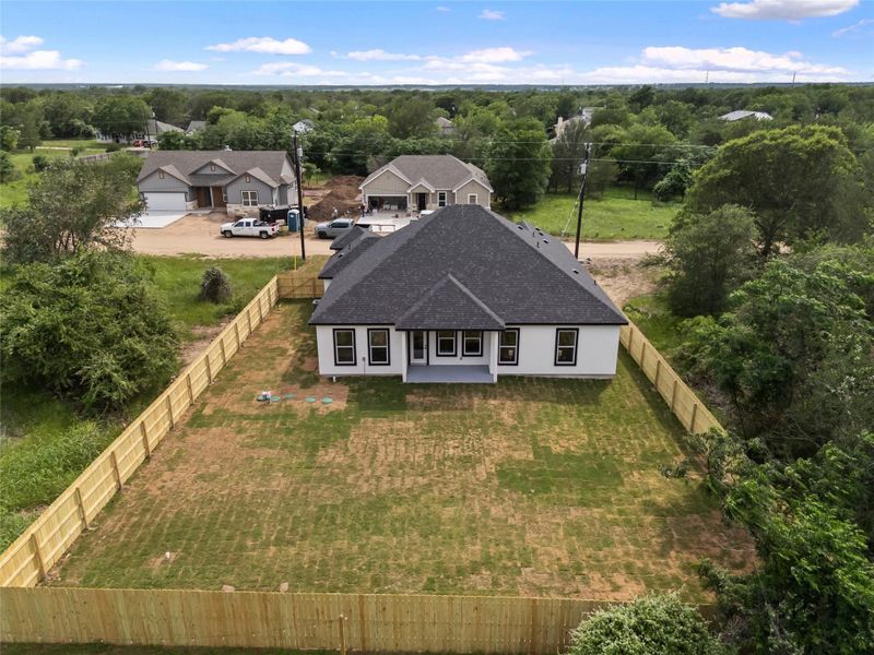 Newly constructed residence featuring a white exterior, dark shingle roof, and a fully fenced backyard