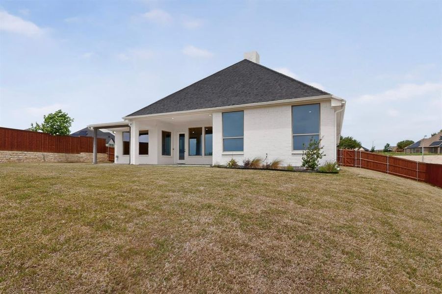 Rear exterior featuring a covered patio, multiple large windows, white brick facade, and a dark shingle roof Rear exterior featuring a covered patio, multiple large windows, white brick facade, and a dark shingle roof