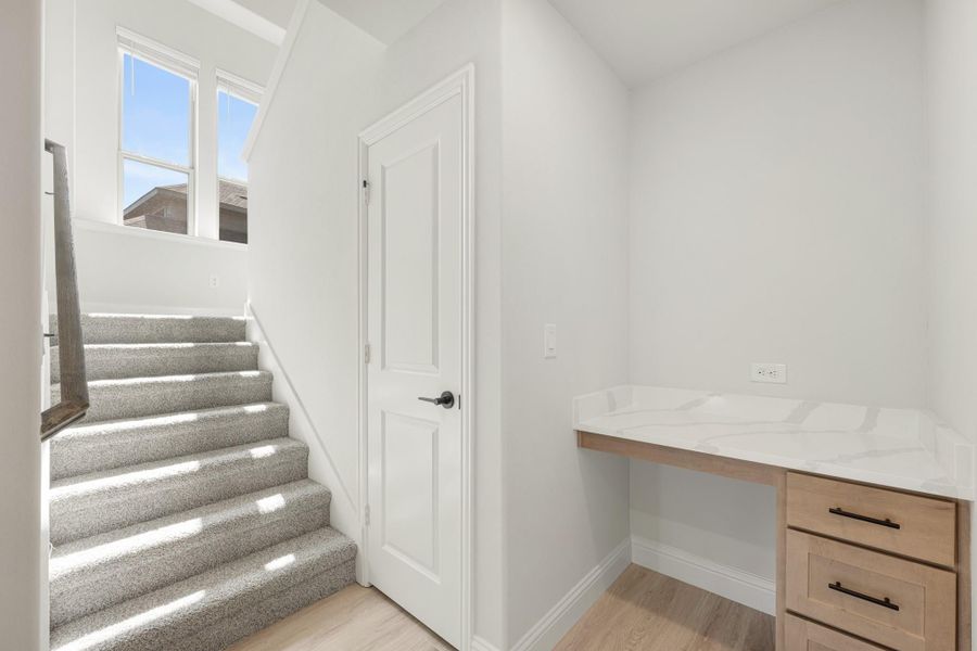 Carpeted staircase next to a built-in wood desk with white quartz countertop and drawers in a bright hallway