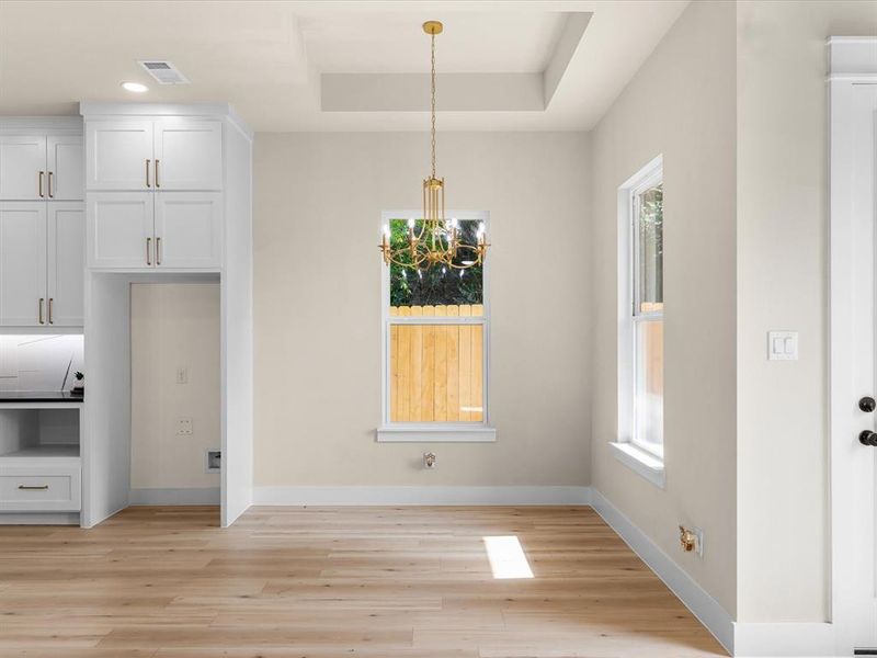 Open-concept living space featuring wood-finish flooring, white cabinetry with gold hardware, a brass chandelier, and recessed lighting