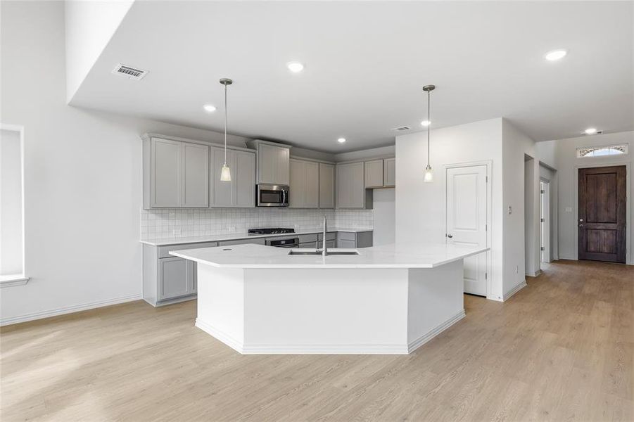 Kitchen with gray cabinets, a kitchen island with sink, stainless steel microwave, and pendant lighting