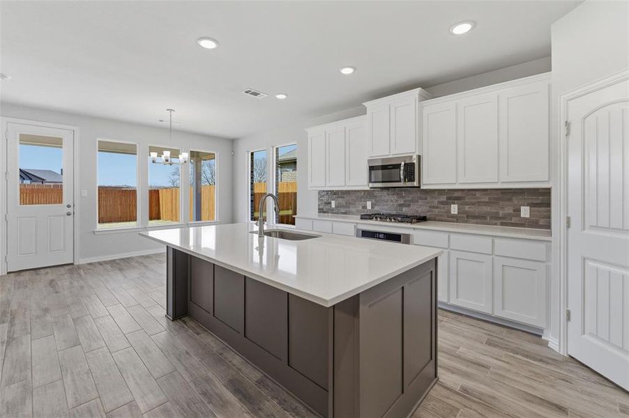 Dual tone kitchen with dual tone cabinets, a center island with sink, light wood finished floors, tasteful backsplash, and hanging lights