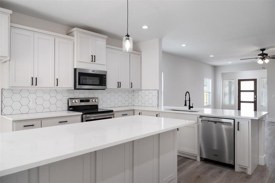 Kitchen with appliances with stainless steel finishes, sink, pendant lighting, decorative backsplash, and wood-type flooring