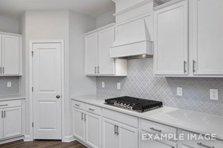 Kitchen with white cabinets, backsplash, light countertops, stainless steel gas cooktop, and custom range hood