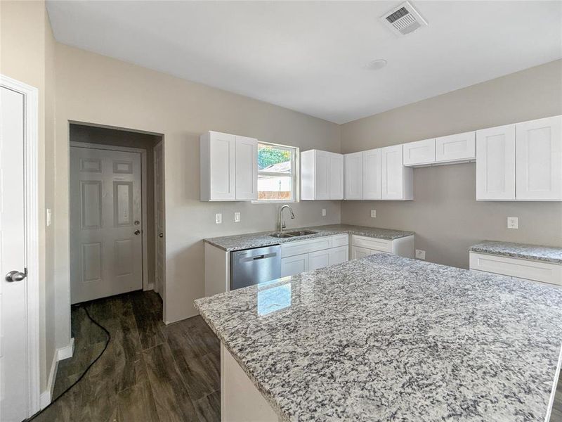 Kitchen with light stone counters, dark wood-type flooring, white cabinetry, and dishwasher