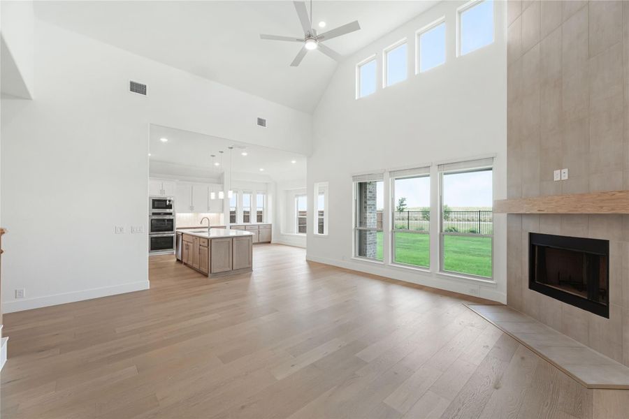 Open living area with vaulted ceiling, tile fireplace, hardwood floors, and open kitchen with island in background.