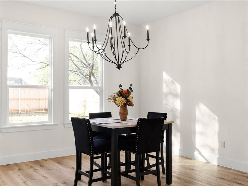 Dining area featuring a dark bronze chandelier, two double-hung windows with white trim, wood-finish flooring, and white baseboards