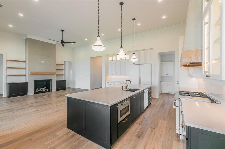 Kitchen with dark cabinetry, light wood-type flooring, decorative light fixtures, white cabinets, and crown molding