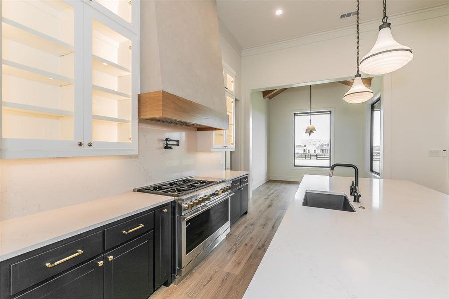 Kitchen featuring dark cabinets, range with two ovens, light stone counters, decorative light fixtures, and light wood-style floors