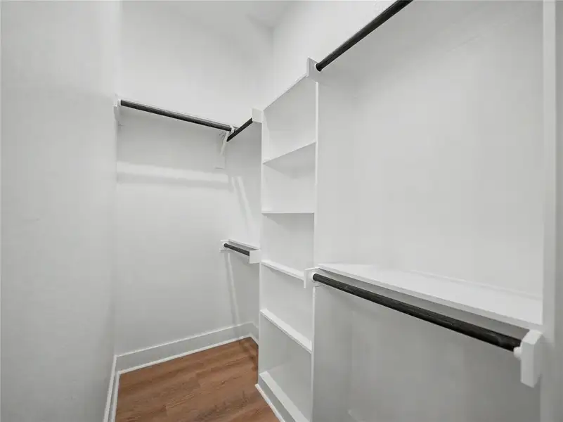 Walk-in closet featuring built-in shelving, multiple hanging rods, white trim, and wood-finish flooring Walk-in closet featuring built-in shelving, multiple hanging rods, white trim, and wood-finish flooring