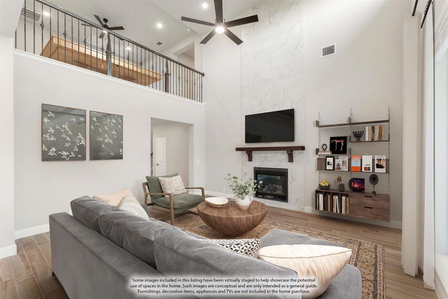 Living room with two-story ceiling, marble fireplace wall, ceiling fan, and open loft railing above