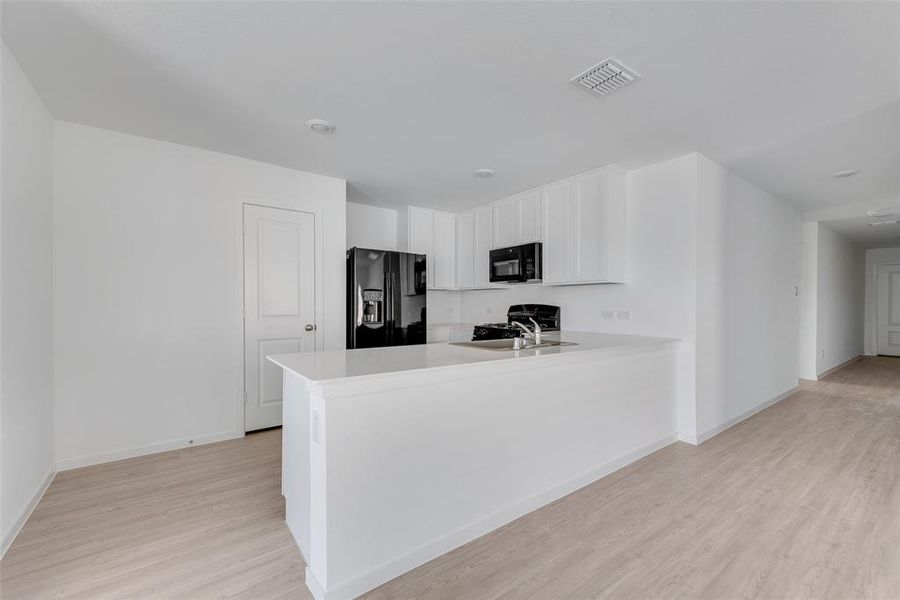 Kitchen featuring sink, kitchen peninsula, white cabinets, black appliances, and light wood-type flooring