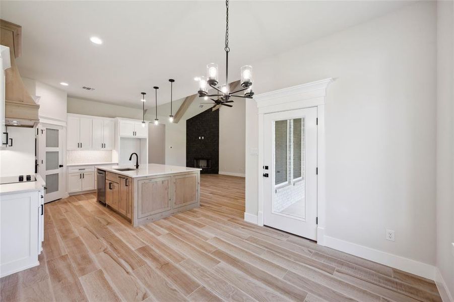 Kitchen with pendant lighting, a kitchen island with sink, sink, light hardwood / wood-style floors, and white cabinetry