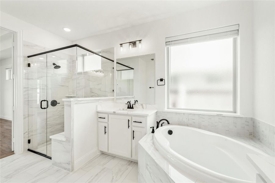 Master bathroom with glass walk-in shower, soaking tub, white vanity, and marble tile throughout