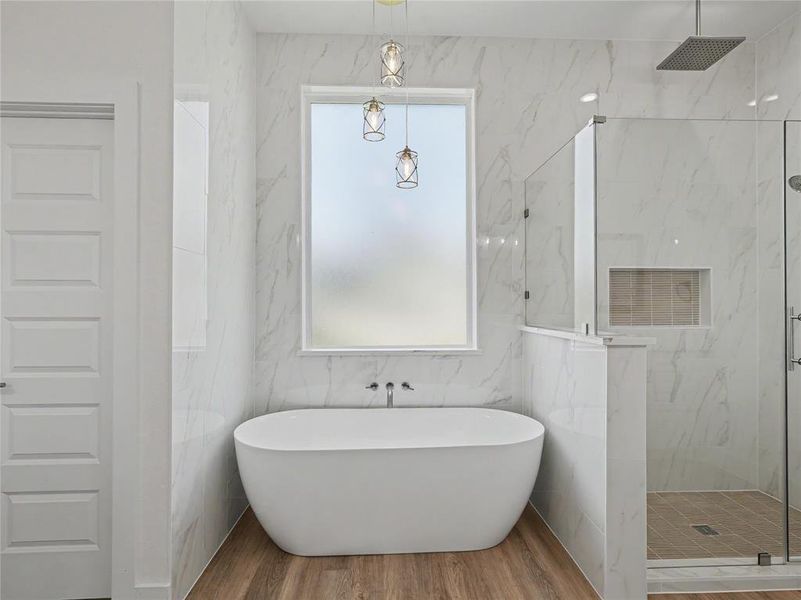 Spacious bathroom featuring a freestanding soaking tub with wall-mounted faucet, a walk-in shower with glass enclosure, and wood-finish flooring