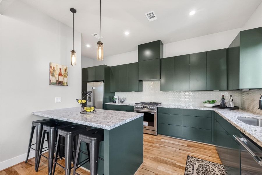 The chef's kitchen is a standout feature of this home. Dark flat-front cabinetry runs floor to ceiling, complemented by stone countertops, a tile backsplash, stainless steel gas range, and a large island with seating for four. Hardwood floors and pendant lighting complete the look.