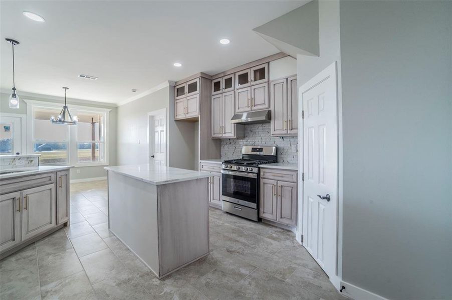 Kitchen featuring stainless steel gas range, a kitchen island, glass insert cabinets, under cabinet range hood, and decorative light fixtures Kitchen featuring stainless steel gas range, a kitchen island, glass insert cabinets, under cabinet range hood, and decorative light fixtures