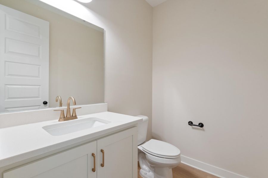 White vanity with cabinet storage, integrated rectangular sink, brushed gold-tone faucet, and a large wall-mounted mirror White vanity with cabinet storage, integrated rectangular sink, brushed gold-tone faucet, and a large wall-mounted mirror