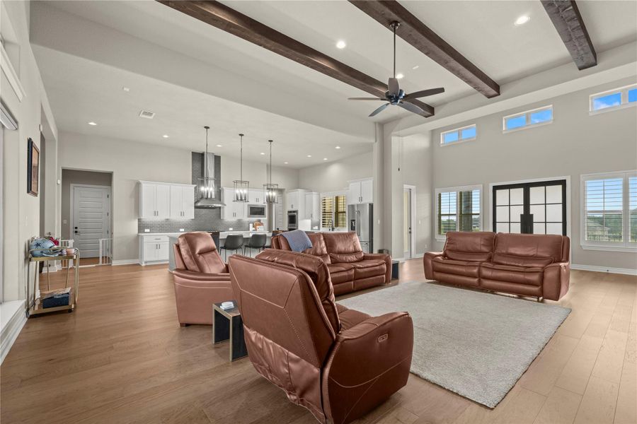 An open-concept living area with soaring ceilings, exposed wooden beams, and abundant natural light flows seamlessly into a modern kitchen. An open-concept living area with soaring ceilings, exposed wooden beams, and abundant natural light flows seamlessly into a modern kitchen.