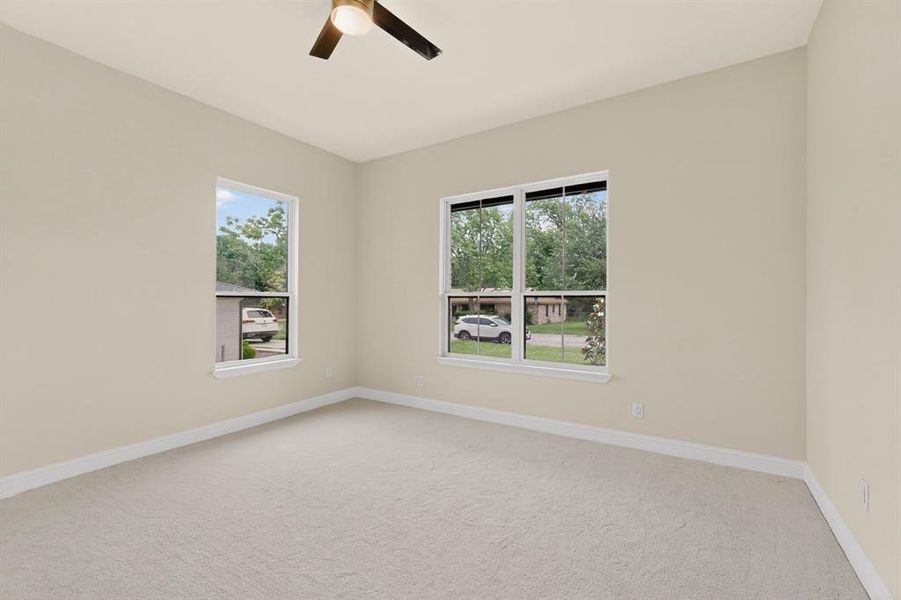 Neutral-toned room featuring a ceiling fan with light, two windows, wall-to-wall carpeting, and baseboard trim
