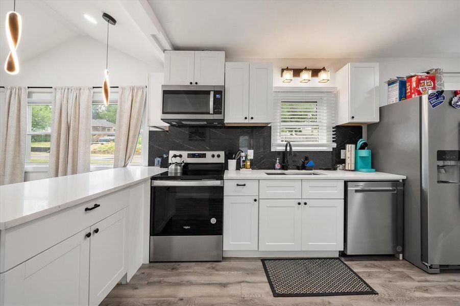 Kitchen featuring stainless steel appliances, light countertops, white cabinetry, decorative backsplash, and vaulted ceiling Kitchen featuring stainless steel appliances, light countertops, white cabinetry, decorative backsplash, and vaulted ceiling