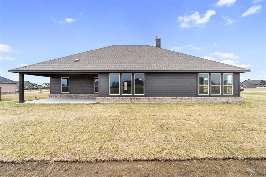 Rear view of house featuring a yard, a patio area, a shingled roof, brick siding, and a chimney