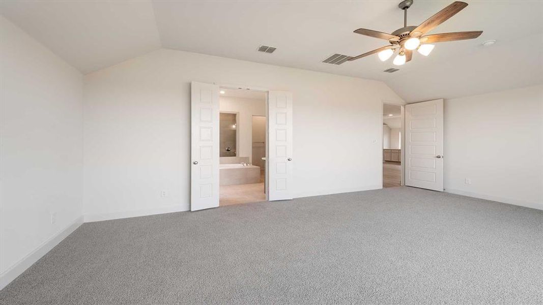 Unfurnished bedroom featuring carpet flooring, vaulted ceiling, ensuite bathroom, and ceiling fan