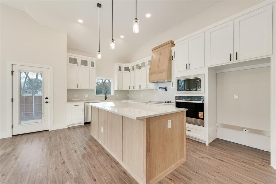 Kitchen featuring stainless steel appliances, a kitchen island, light brown cabinetry, glass insert cabinets, and custom exhaust hood